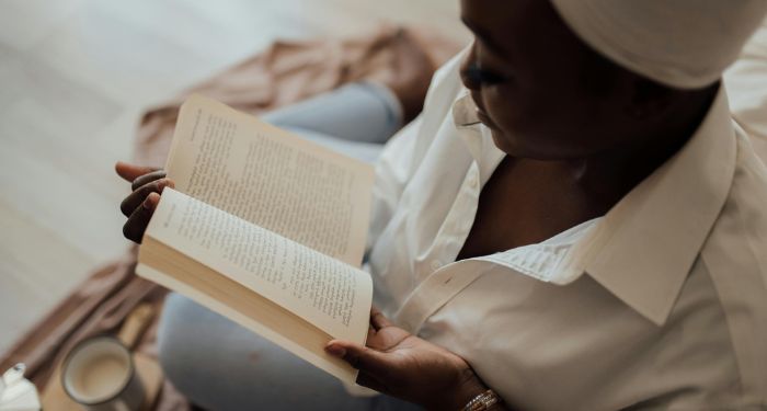 brown skinned Black woman with a head wrap reading a book.jpg.optimal